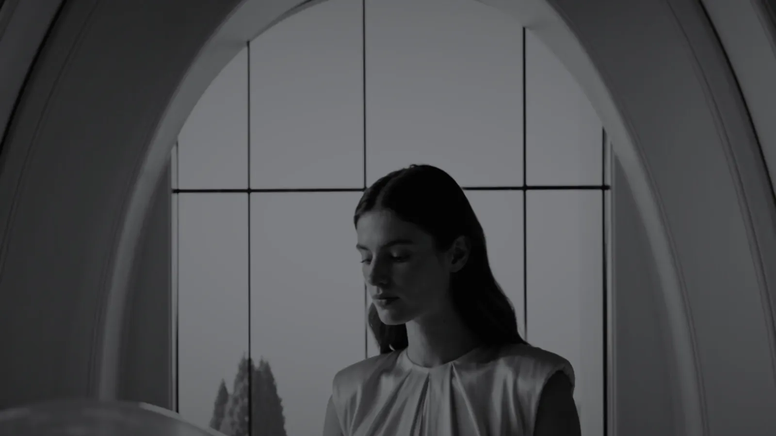 Figure framed by a tall arched window, in black and white